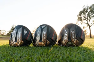 Three Srixon ZX5 drivers are placed side by side on a grassy field with trees in the background. The drivers, black with white and red accents, are angled facing forward. The sun is setting or rising, casting a warm glow over the scene, creating an idyllic backdrop for this Srixon ZX5 driver review.