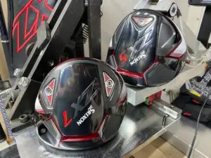 Close up of two black Srixon ZX golf club heads placed on a piece of golf equipment likely for customization or adjustment The club heads featuring red and white accents are seen in a well lit setting with other equipment nearby reminiscent of a detailed driver review scene