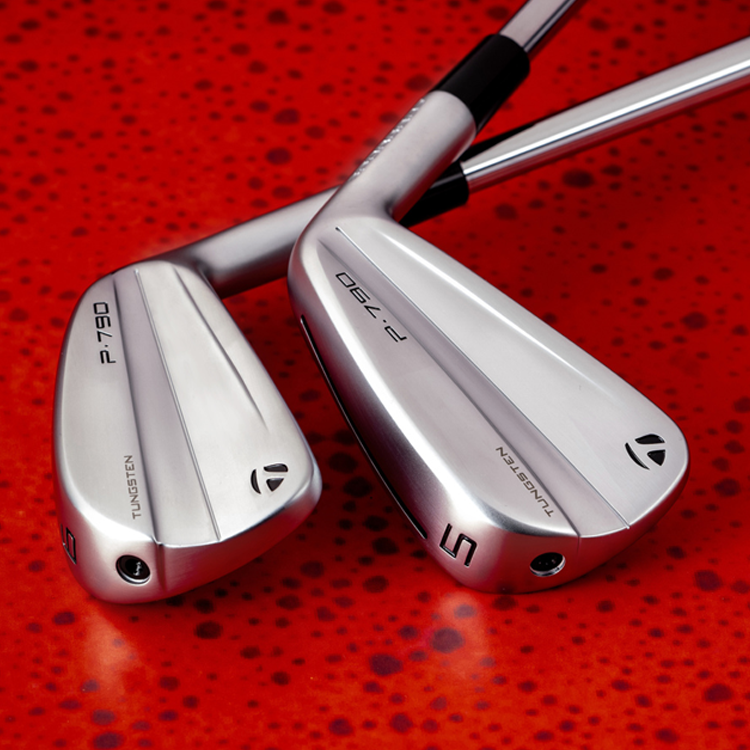 Close-up of two golf clubs placed on a red speckled surface. The clubs are labeled "P-790" and "5" with tungsten inserts.