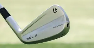 Silver golf iron with Tungsten and P  engraved on its back against a blurry green background this TaylorMade club is designed to elevate your game