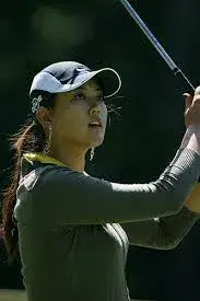 A rising star in the golf  scene the person dons a cap and earrings holding a golf club while gazing into the distance during a swing