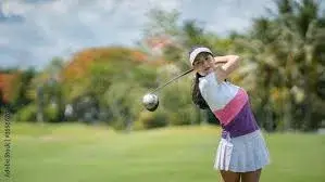 A rising star among Asian golfers dressed in a stylish white and pink outfit is mid swing on the lush green course framed by trees in the background It's 2025, and their talent is shining brighter than ever.