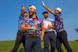 Four men wearing colorful Golf Polo Brands shirts celebrate on a golf course under a clear blue sky