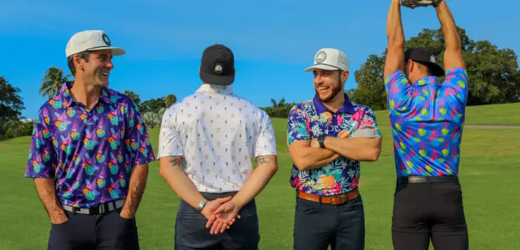 Four men wearing vibrant golf shirts, showcasing some of the best golf polo brands, stand together on a lush golf course. The backdrop features tall trees and a clear blue sky.