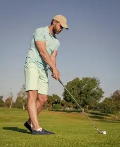 A man in a light blue shirt and shorts perfects his golf stance as he prepares to hit a ball on a sunny day Standing on the lush green course he's focused on improving his game with these simple steps.