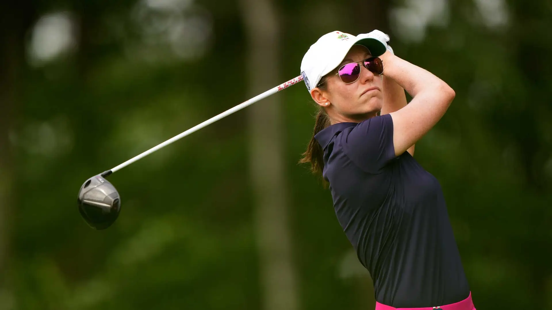 A golfer in a navy shirt and white cap expertly swings a golf club outdoors, showcasing the best of left-handed golf sets designed for women.