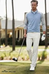 A person in stylish Peter Millar golf attire walks on a lush golf course holding a club There's a house in the background.