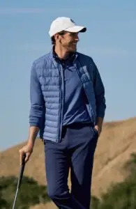 A person in a stylish blue outfit and white cap holds a golf club while standing outdoors on a sunny day embodying the essence of luxury apparel