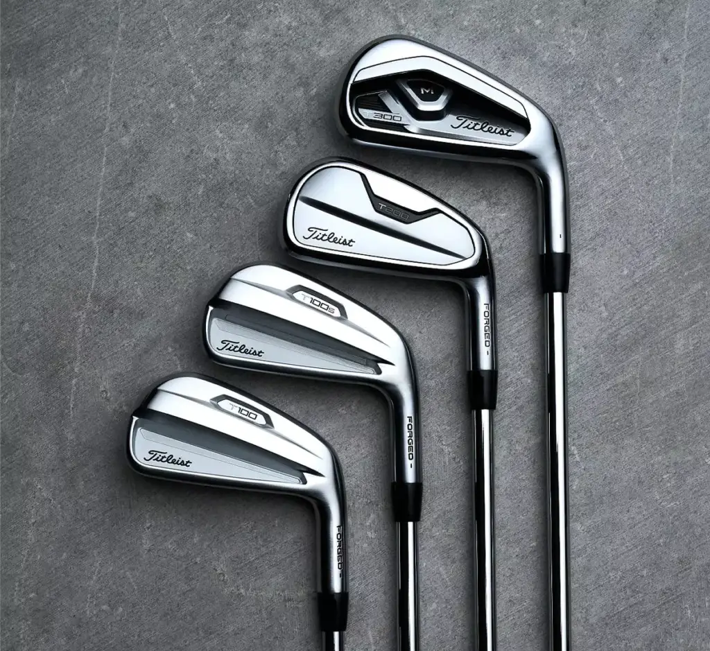 Four silver golf clubs considered among the best golf irons with black and white grips are laid out on a gray surface presenting a sleek vision of 